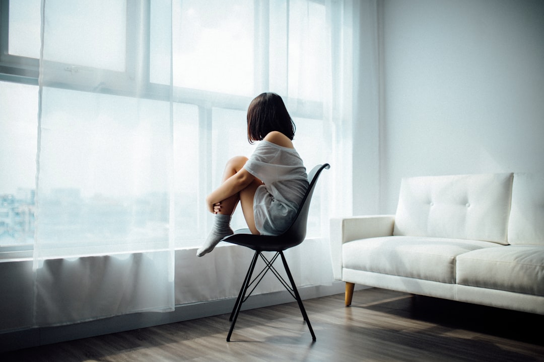 woman-sitting-on-black-chair-in-front-of-glass-panel-window-with-white-curtains-vxymirxr5ac
