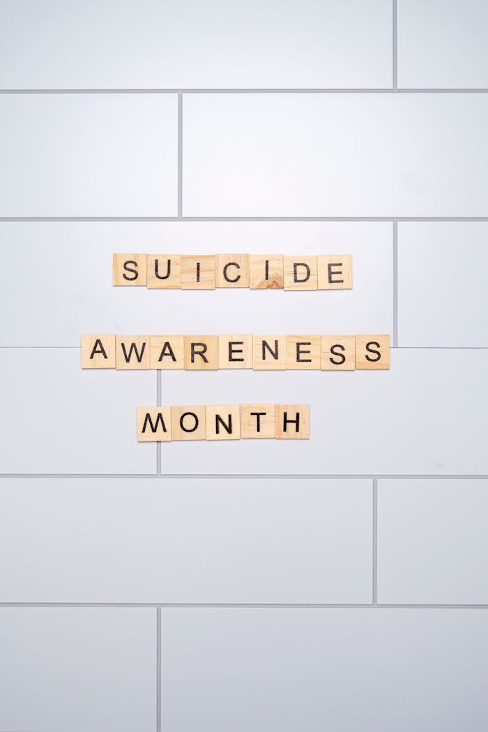 Scrabble letters spelling Suicide Awareness Month on clean tiled wall background.